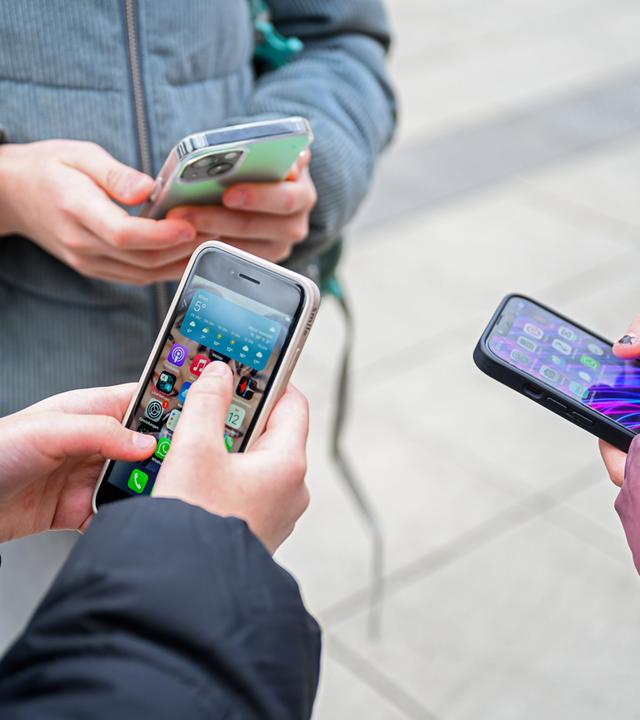 Drei Schülerinnen stehen mit Handys beisammen.