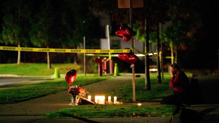Vor dem Tatort an einer Grundschule in Oregon wurden in gedenken an die Opfer Luftballons und Kerzen aufgestellt. Eine Person kniet vor der Gedänkstätte.