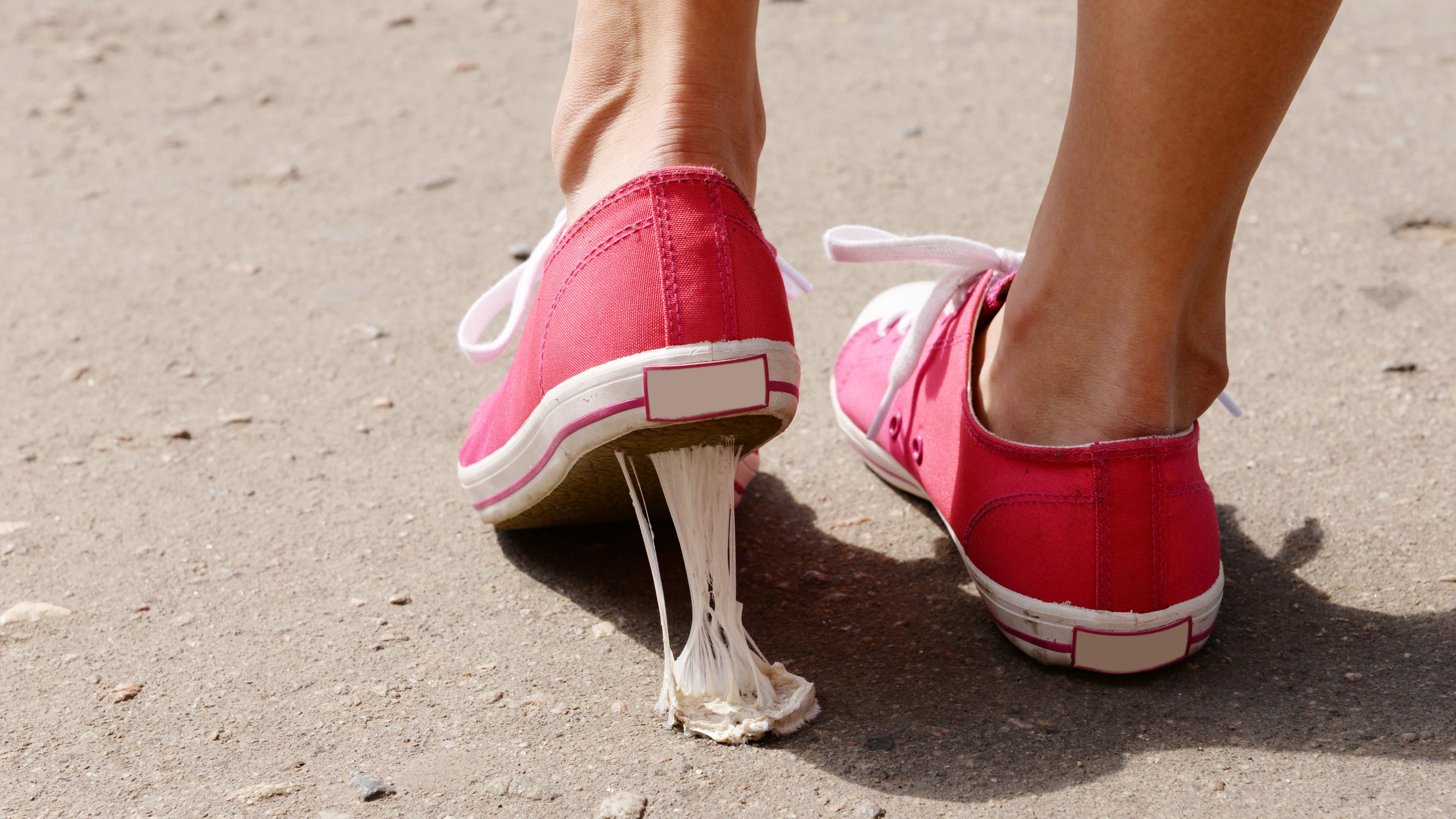 Ein Kaugummi klebt beim anheben des Fußes an der Sohle eines roten Sneaker.