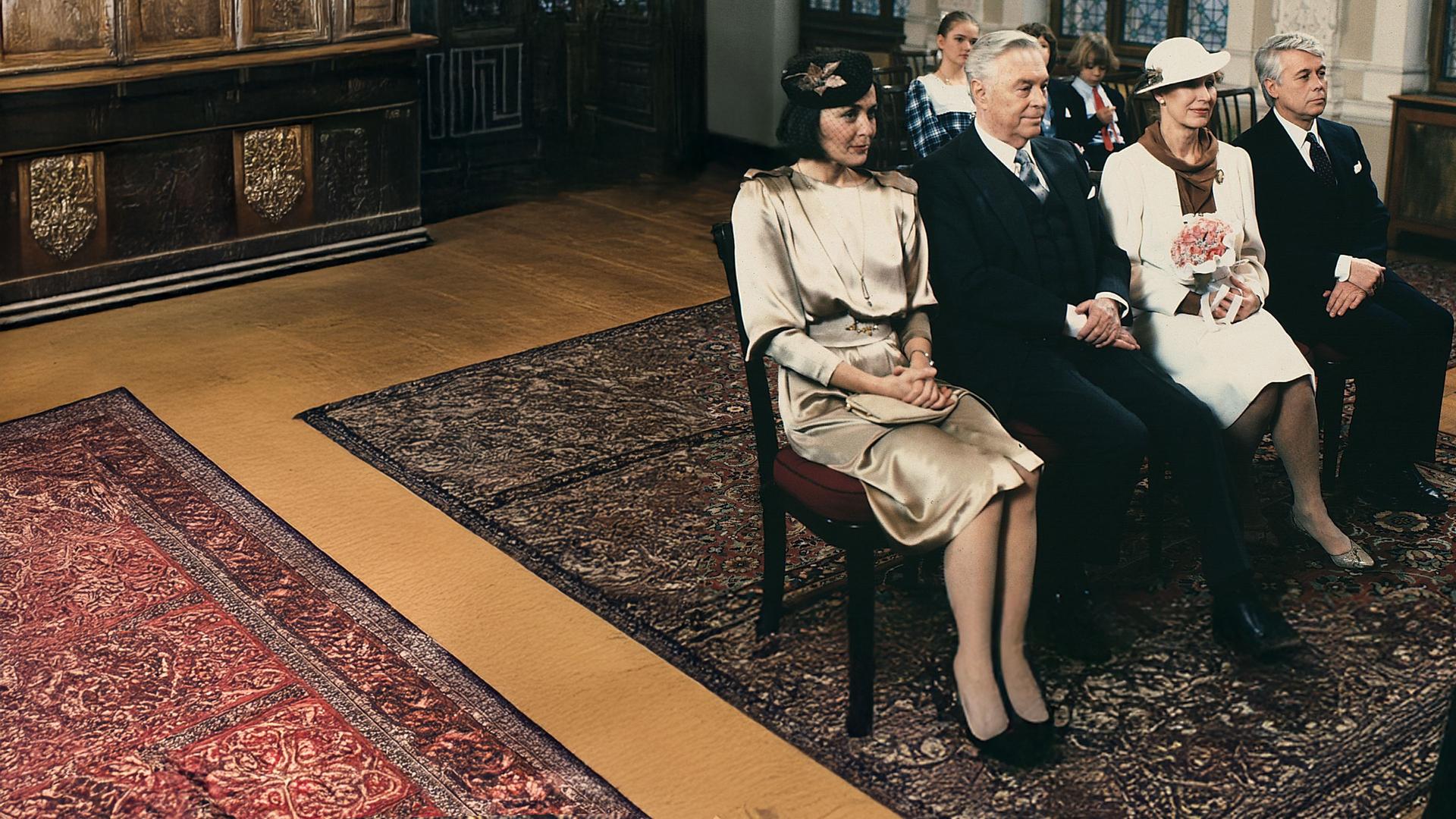 Werner und Angi sitzen in Abendgarderobe mit Onkel Rudolf und seiner Braut in einer Stuhlreihe im Saal des Standesamts. Im Hintergund sitzen die drei Kinder. 