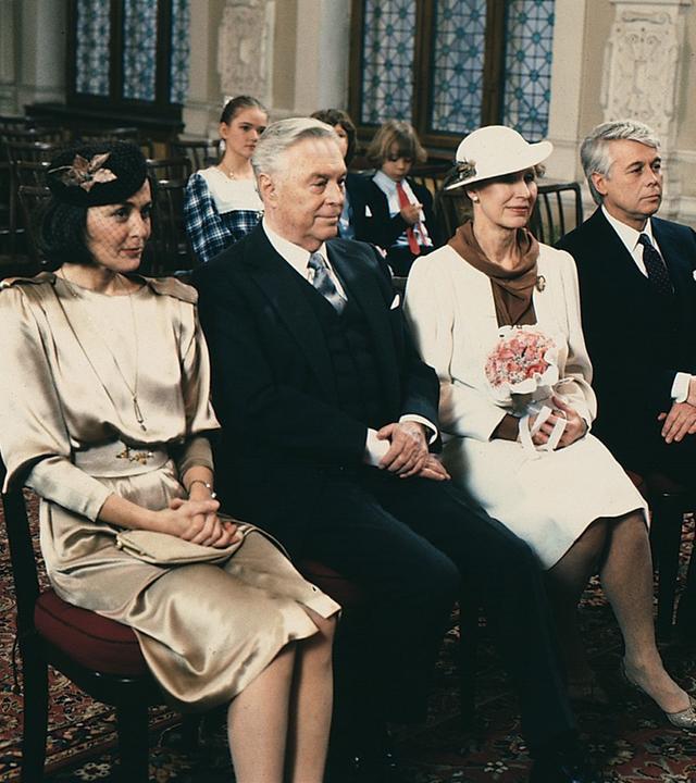 Werner und Angi sitzen in Abendgarderobe mit Onkel Rudolf und seiner Braut in einer Stuhlreihe im Saal des Standesamts. Im Hintergund sitzen die drei Kinder. 