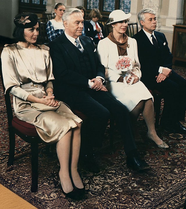 Werner und Angi sitzen in Abendgarderobe mit Onkel Rudolf und seiner Braut in einer Stuhlreihe im Saal des Standesamts. Im Hintergund sitzen die drei Kinder. 