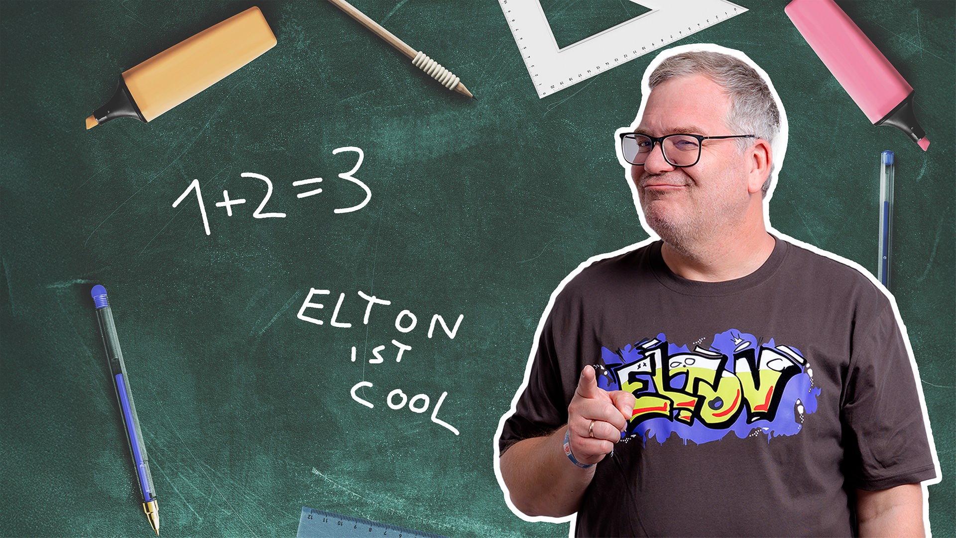 Moderator Elton zeigt vor einer grünen Schultafel nach vorn. Darauf stehen „1 + 2 = 3“ und „Elton is cool“.