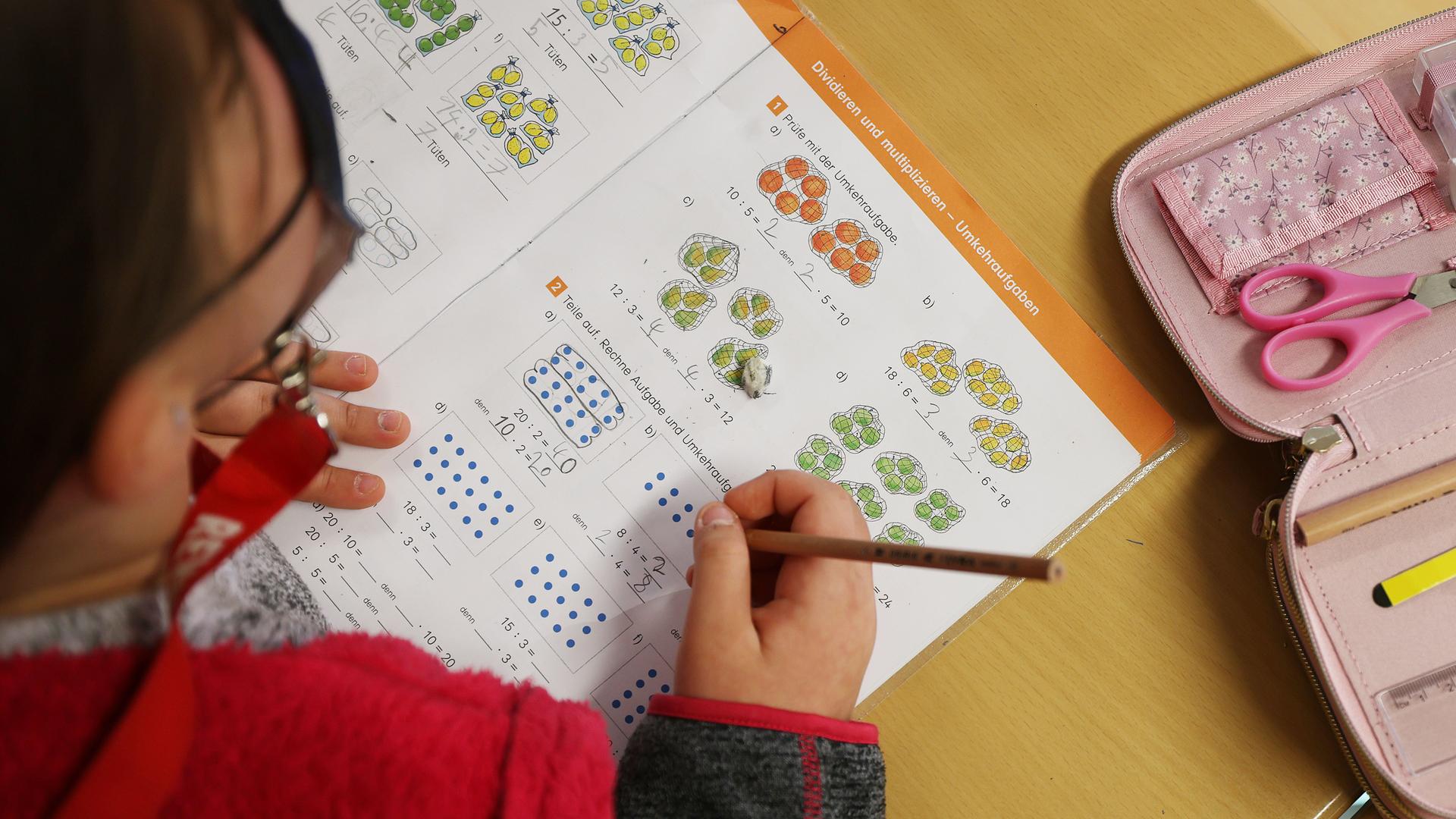 Eine Schülerin schreibt im Unterricht in ihr Schulbuch und löst eine Rechenaufgabe.