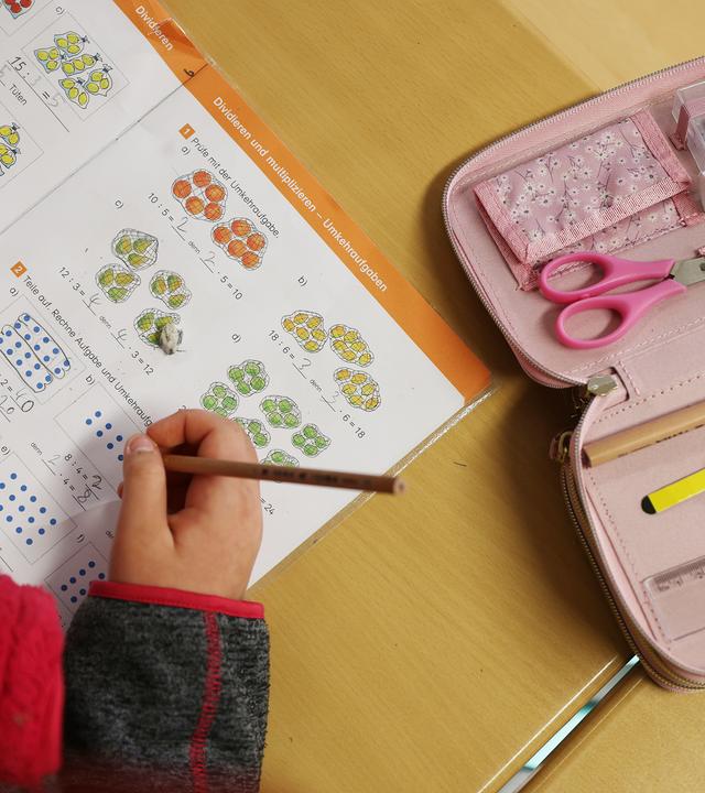 Eine Schülerin schreibt im Unterricht in ihr Schulbuch und löst eine Rechenaufgabe.