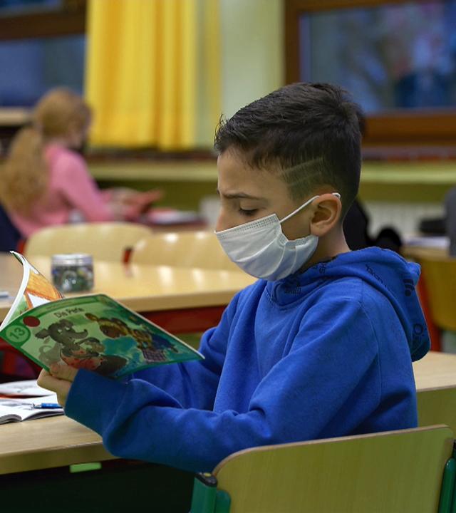 Schulkind mit Maske schaut sich ein Heft an 