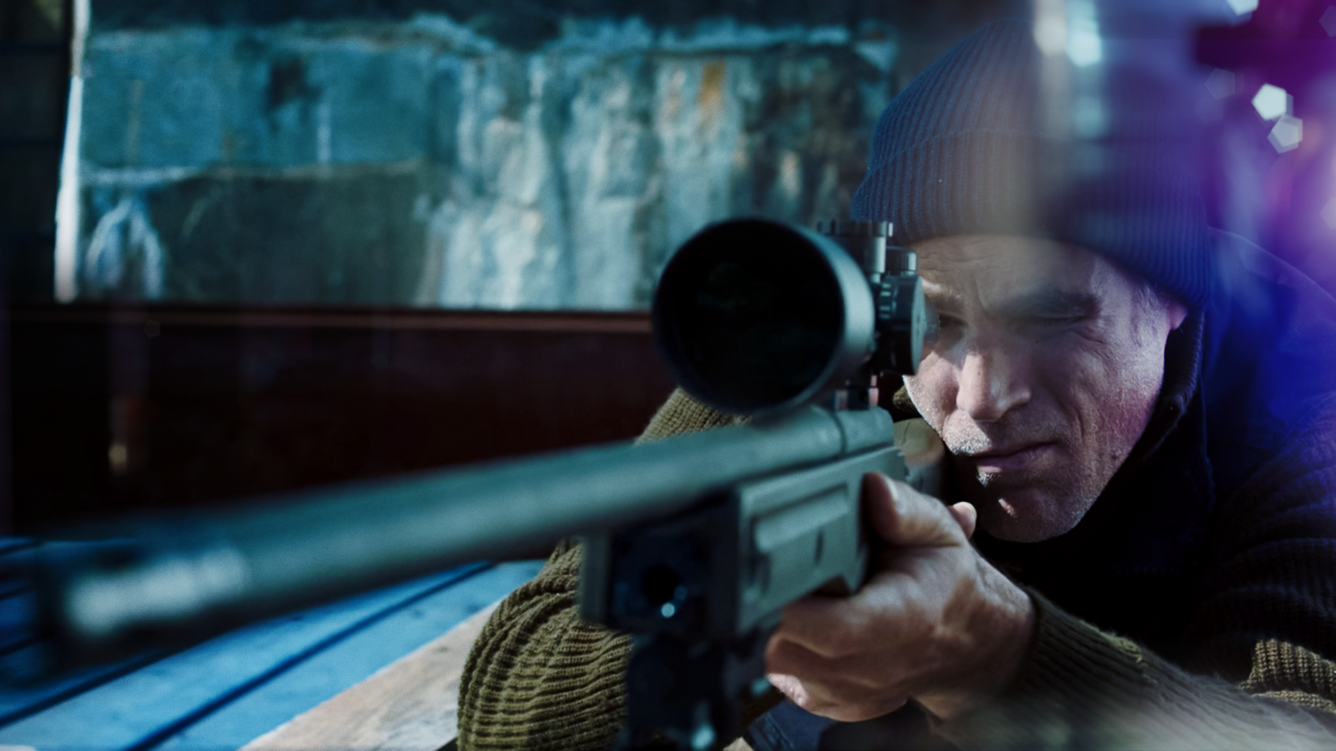 Ein Mann steht im Dunklen vor einem Fenster und setzt zum Schuss mit seiner Waffe an.