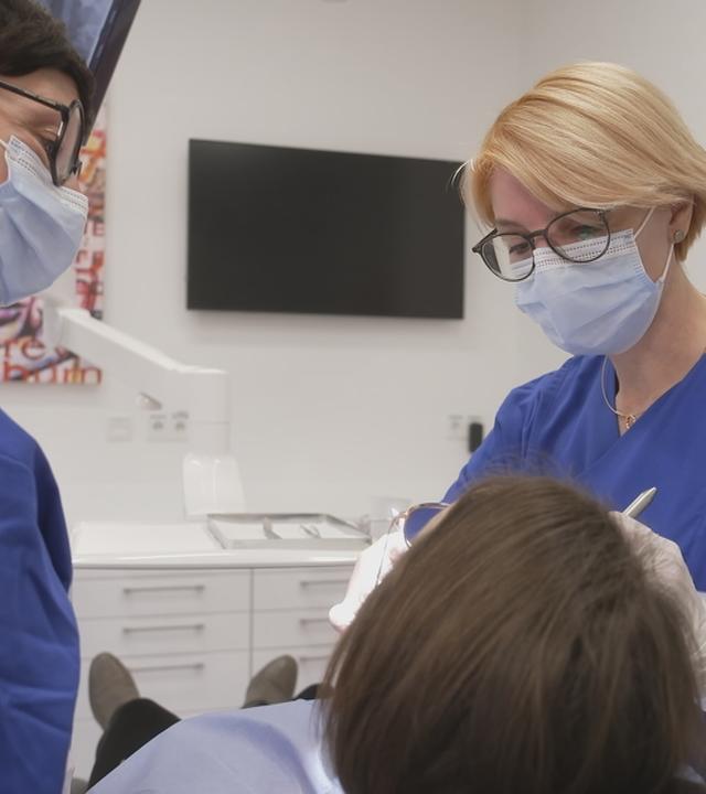 Eine Frau (von hinten zu sehen) auf einem Stuhl in Behandlung beim Zahnarzt.