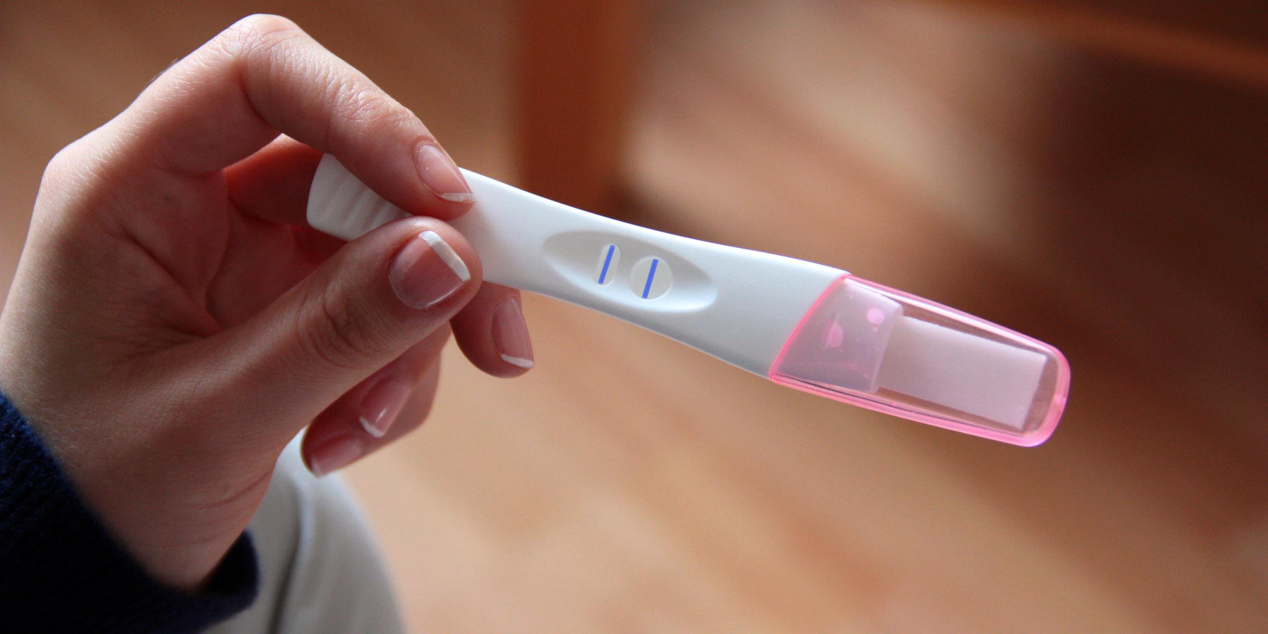 Das Bild zeigt eine Frau, die einen positiven Schwangerschaftstest in der Hand hält.