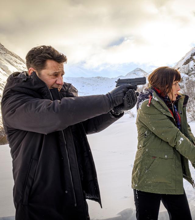 Constance Vivier (Clémentine Poidatz) auf der Rechten und Andreas Meyer ( Laurent Gerra) auf der Linken. Im Hintergrund eine Schneelandschaft. Beide haben ihre Waffe in der Hand und zielen auf eine Person außerhalb des Bildes.