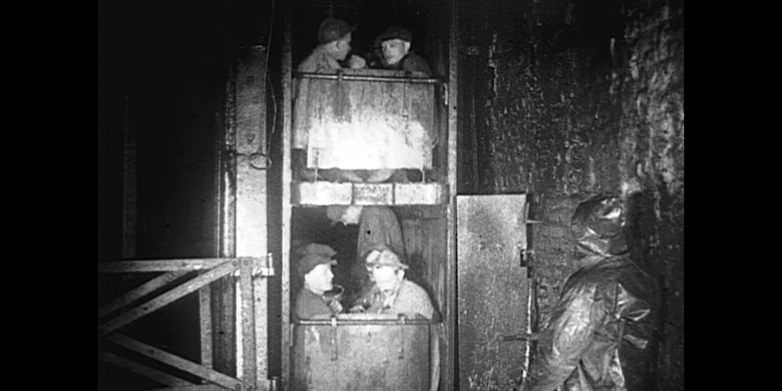 Bergarbeiter im Bergstollen sitzen in zwei übereinander liegenden Schachtwagen. Schwarz-weiße Fotografie