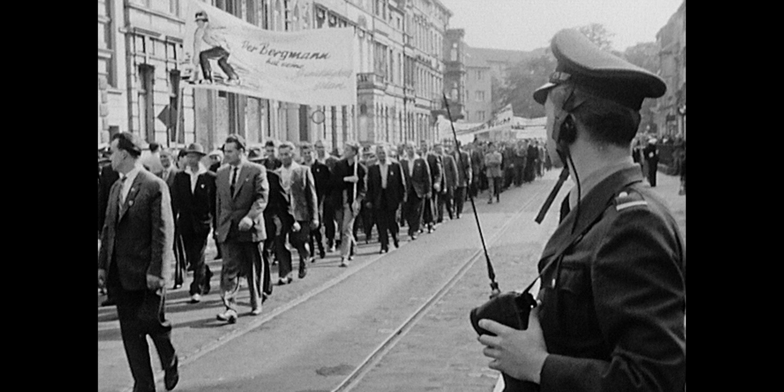Schwarz-weiß Fotografie einer Menge an Demonstranten, rechts im Bild ein Polizist. 