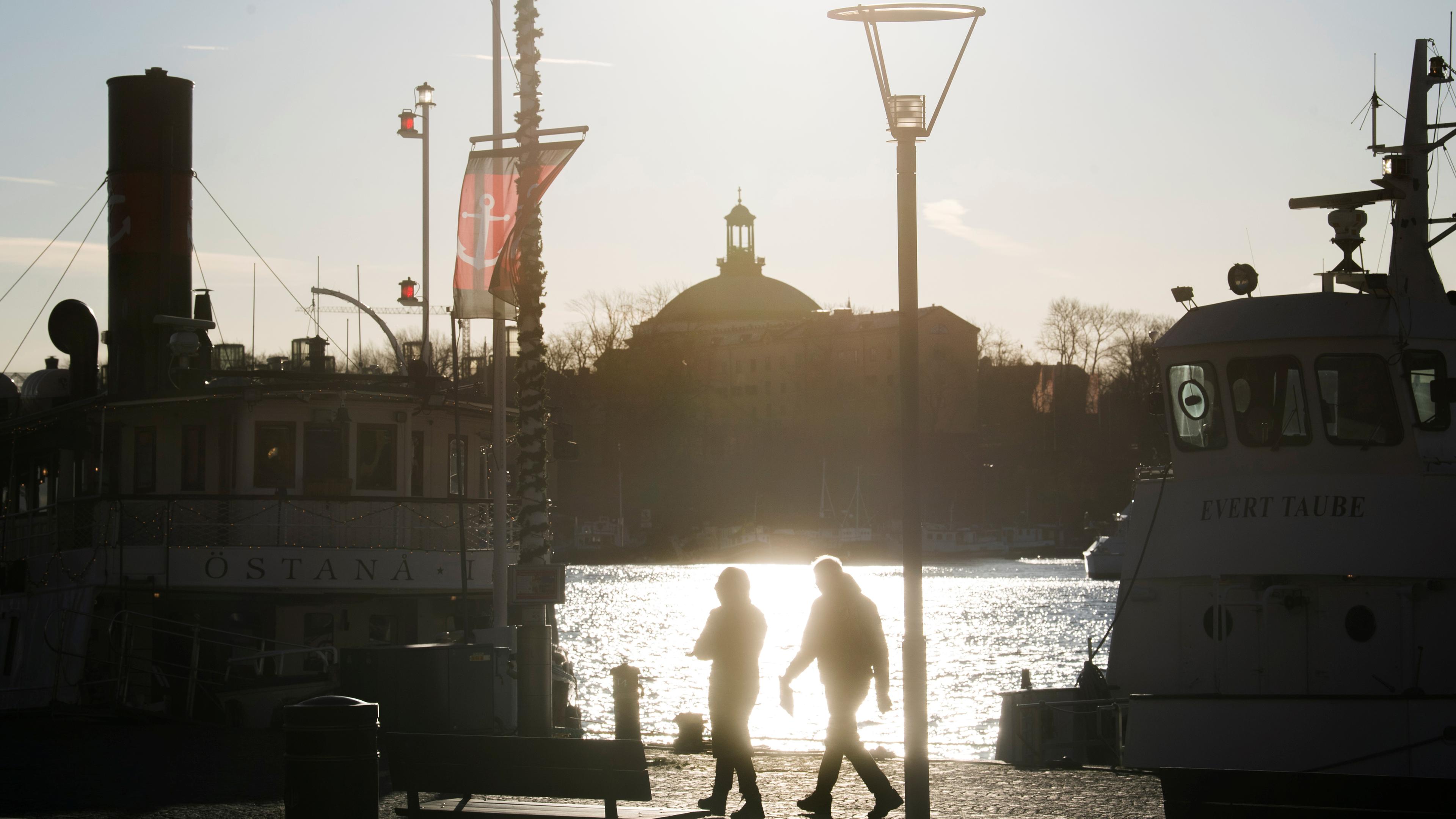 Zwei Menschen laufen an einer Hafenbucht in Schweden entlang.