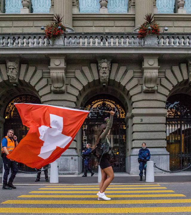 Eine Frau geht über die Straße mit einer Schweizer Fahne in der Hand.