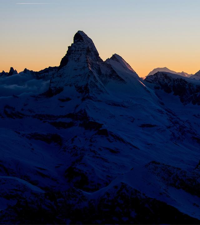 Die Silhouette des Matterhorns vor einem orangefarbenen Himmel in der Abenddämmerung.