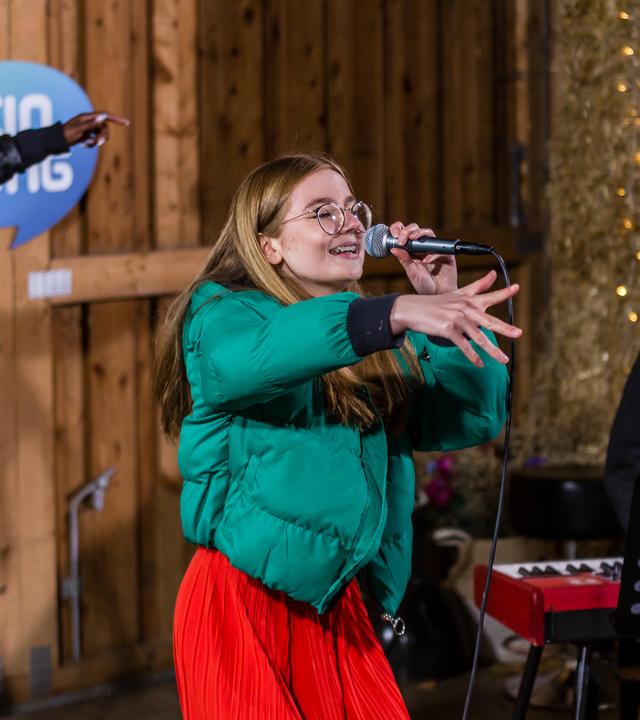 "Dein Song" Kandidatin Fine steht mit dem Mikrofon in der Hand, singend in der "Dein Song" Scheune und streckt ihre rechte Hand nach vorne.