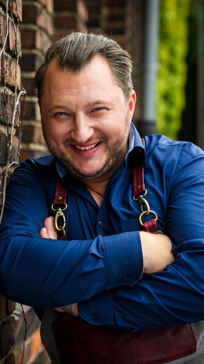 Halbtotale Foto von Koch Sebastian Lege, verschränkte Arme, Lächeln, lehnt an einer Mauer 