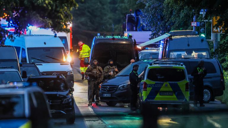 Auf einer Straße stehen mehrere Polizweiwagen und andere Einsatzwagen, es sind bewaffnete Einsatzkräfte des SEK zu sehen, mehrere Polizisten und ein Rettungssanitäter
