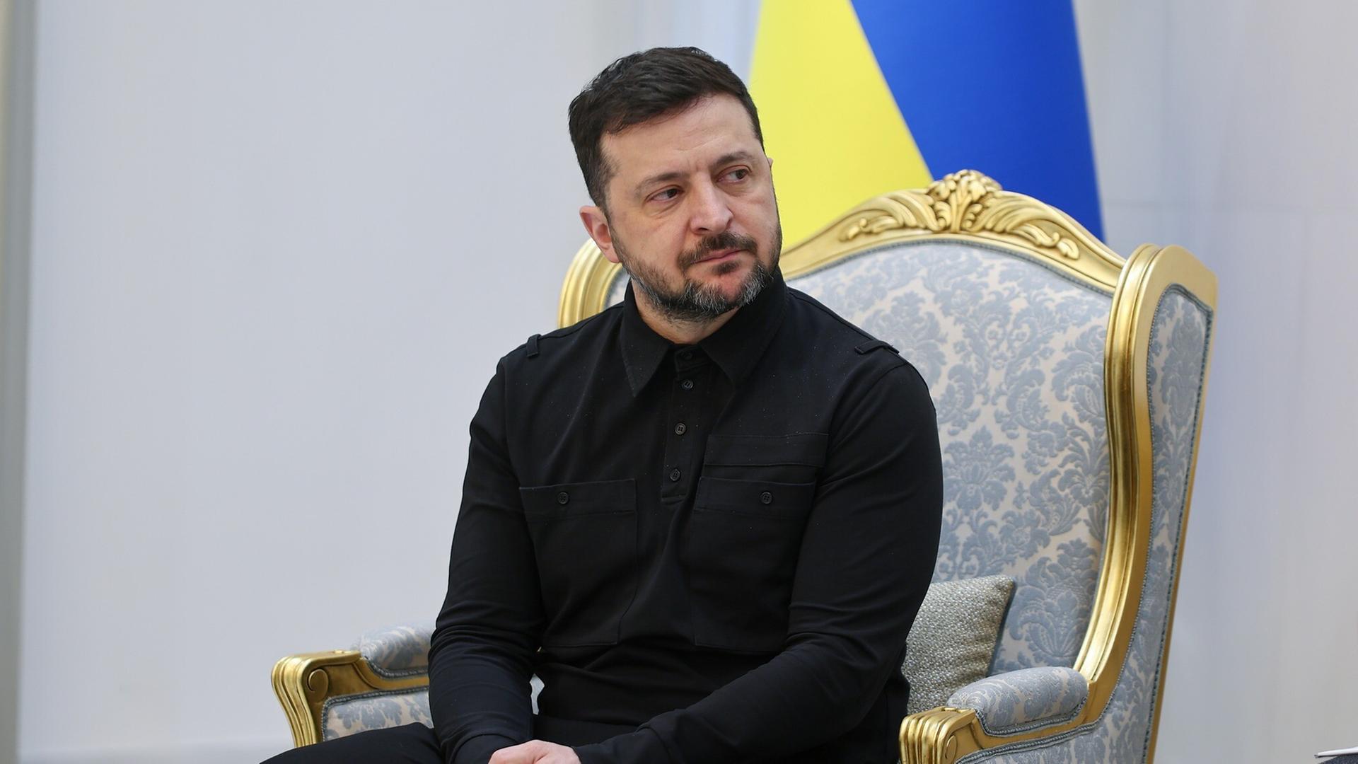 Wolodymyr Selenskyj sitzt vor einer Ukraine-Flagge.