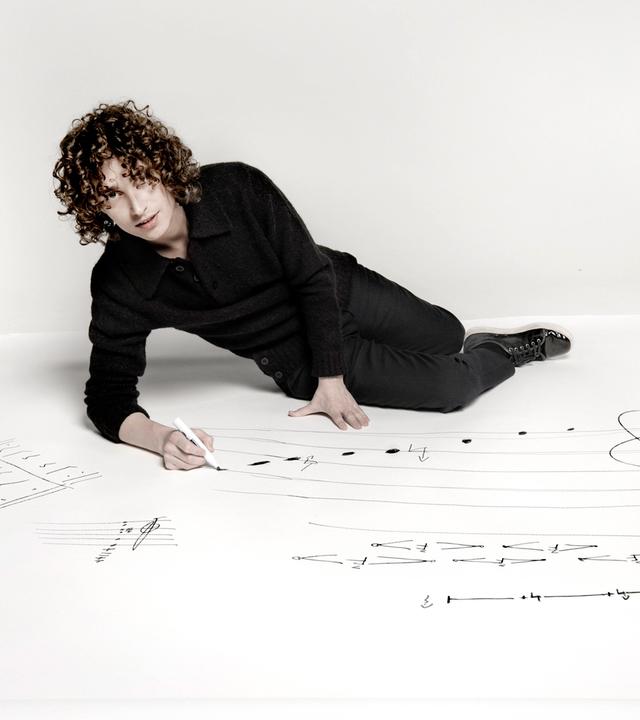 Ein junger Mann liegt auf einem weißen Boden und schreibt mit Edding Noten.