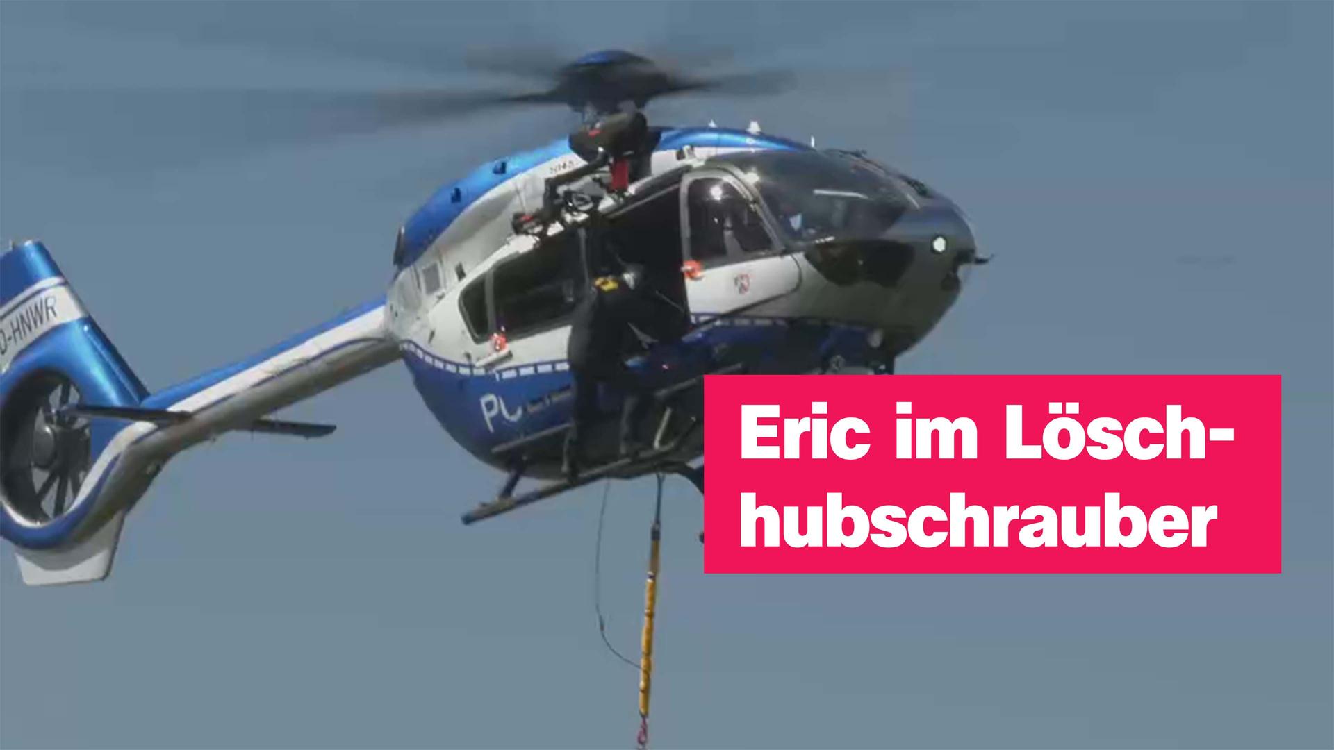 Ein blau-silberner Hubschrauber fliegt in der Luft, eine Person klettert aus der Tür hinaus und hält sich an der Außenseite fest. Rechts der Text "Eric im Löschhubschrauber".