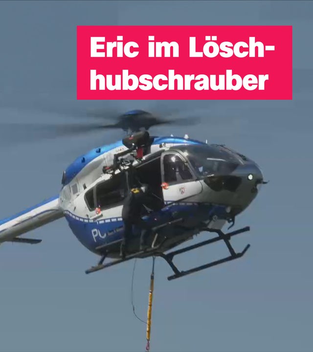 Ein blau-silberner Hubschrauber fliegt in der Luft, eine Person klettert aus der Tür hinaus und hält sich an der Außenseite fest. Rechts der Text "Eric im Löschhubschrauber".