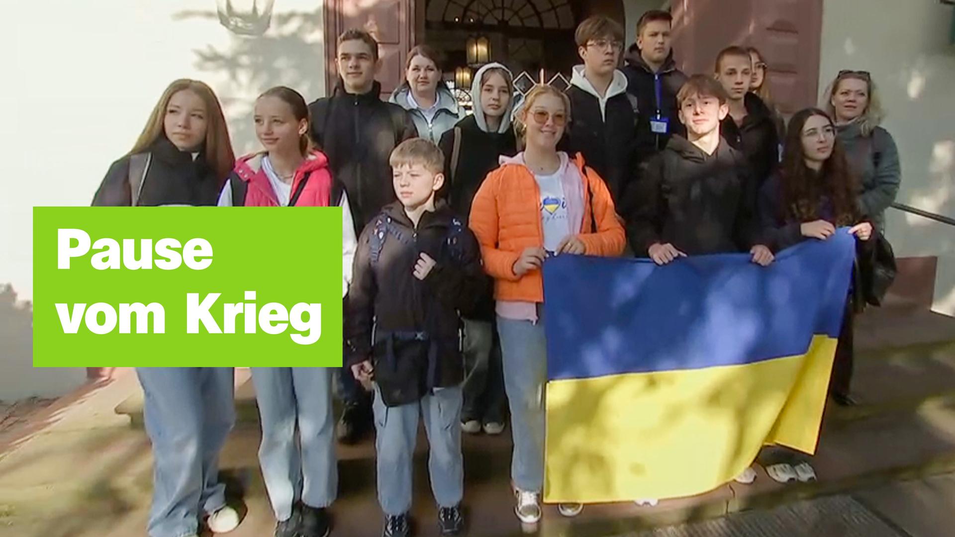 Eine Gruppe von Jugendlichen steht zusammen und hält eine ukrainische Flagge. Links der Text "Pause vom Krieg".