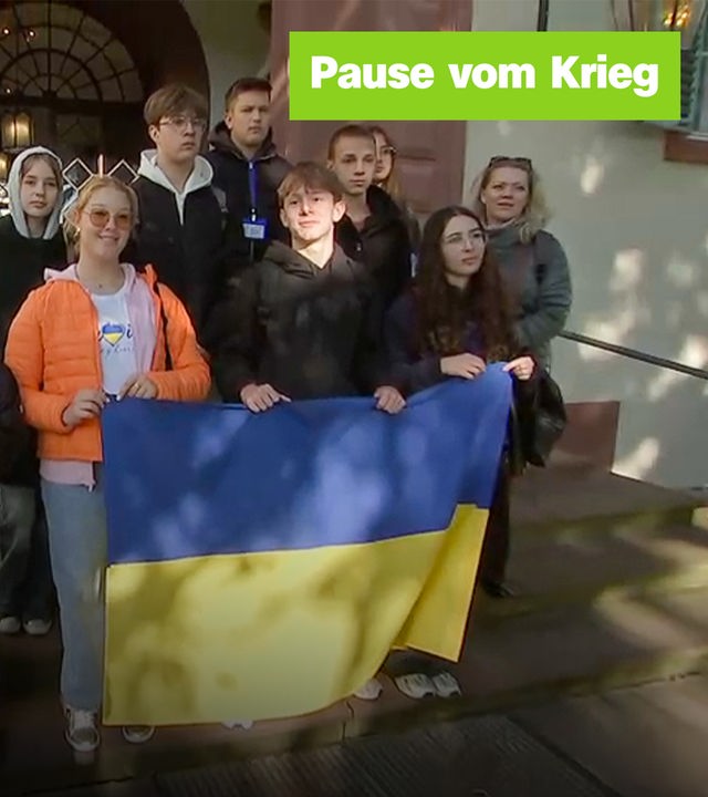 Eine Gruppe von Jugendlichen steht zusammen und hält eine ukrainische Flagge. Links der Text "Pause vom Krieg".