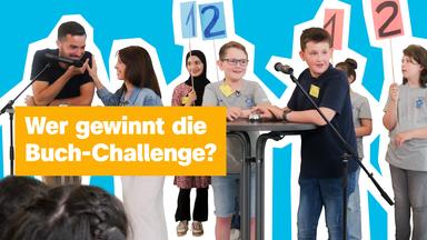 Mehrere Kinder stehen von Mikrofonen umgeben vor Publikum, zwei davon an einem Stehtisch, die anderen halten Schilder mit den Zahlen 1 und 2 hoch, in rot und blau. Links steht ein Moderator, vor dem ein Mikrofon aufgebaut ist. Links der Text: "Wer gewinnt die Buch-Challenge?"