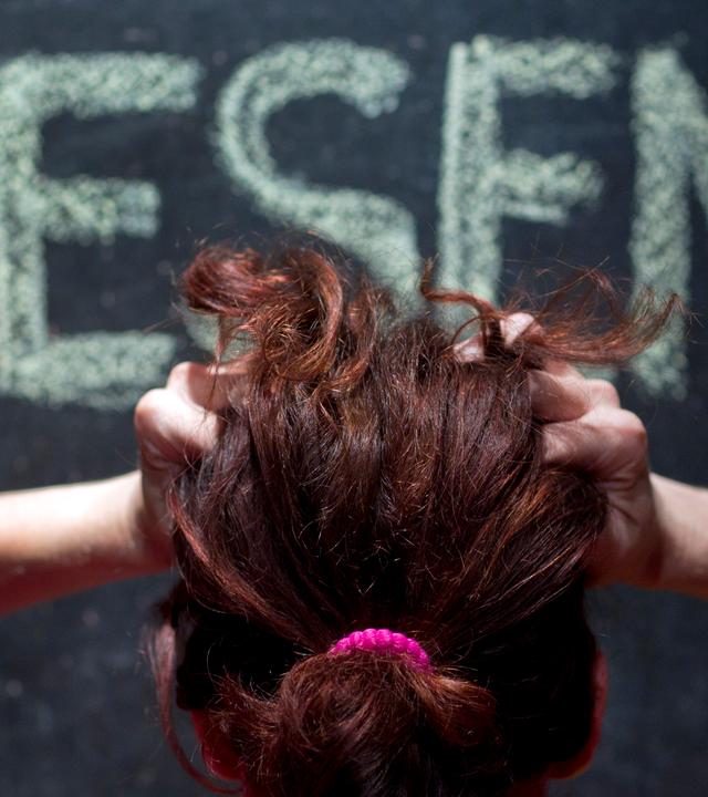 Eine Frau ist von hinten zu sehe, rauft sich die Haare beim Blick auf eine Tafel, auf der das Wort LESEN steht.