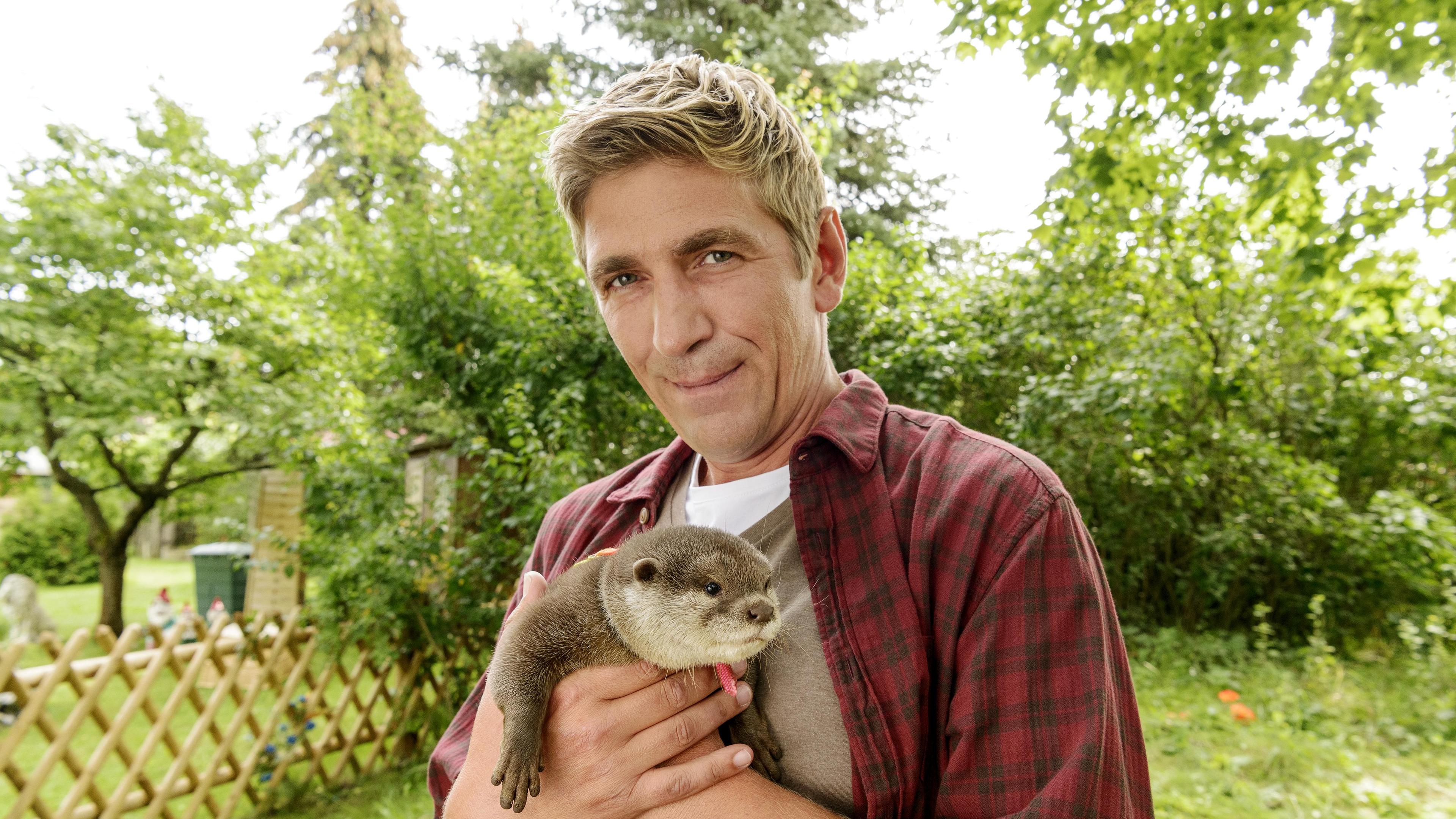 Fritz Fuchs steht im Garten und hält einen Fischotter in den Händen.