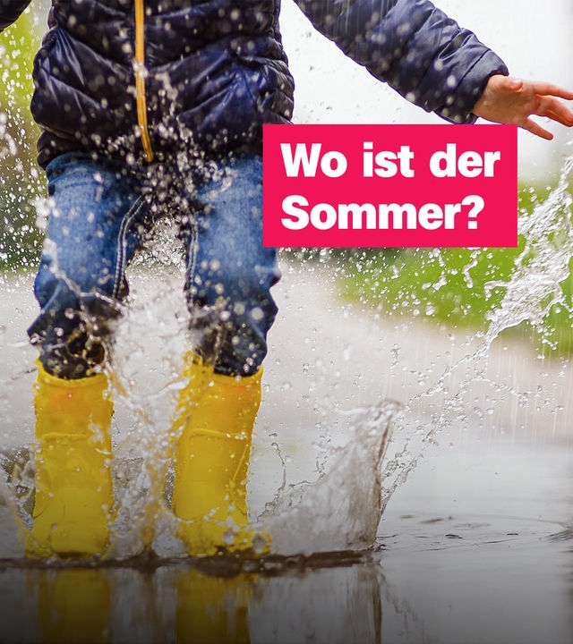 Ein Kind mit gelben Gummistiefeln und blauer Jeans hüpft fröhlich in eine Pfütze. Wasser spritzt hoch, während es eine dunkle Jacke trägt. Rechts im Bild steht der Text „Wo ist der Sommer?“ auf pinkem Hintergrund.