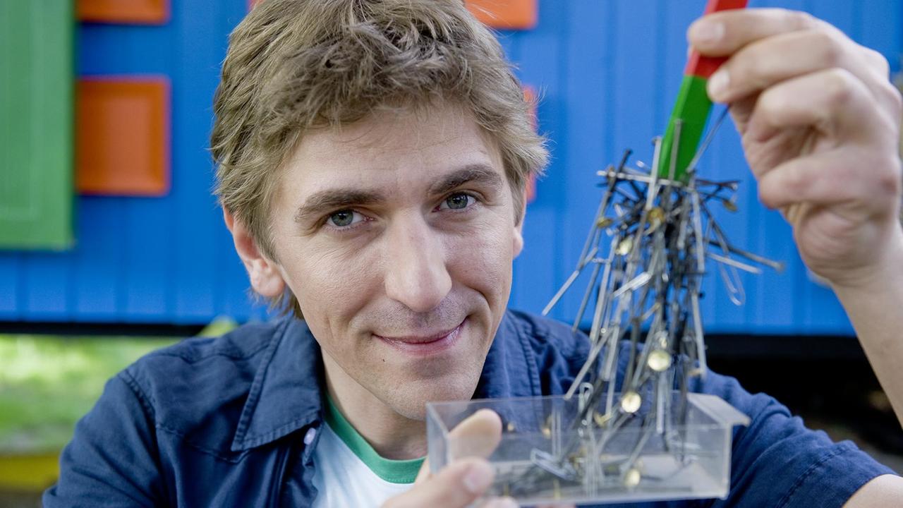Fritz Fuchs mit einem Magnet in der Hand, der Nägel anzieht.