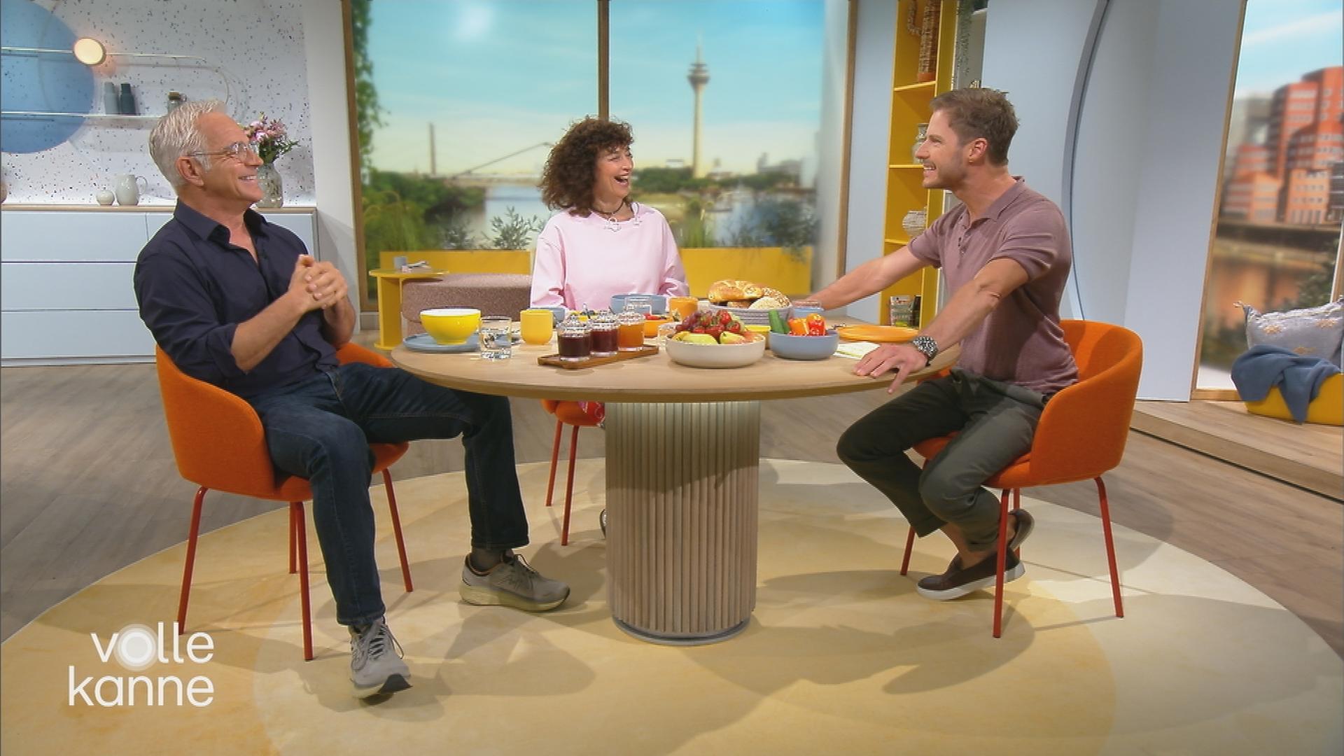 Florian Fitz, Isabel Varell und Florian Weiss sitzen grinsend am "Volle Kanne"-Frühstückstisch