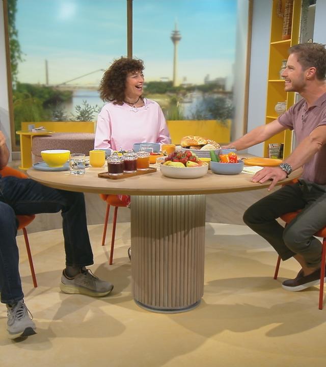 Florian Fitz, Isabel Varell und Florian Weiss sitzen grinsend am "Volle Kanne"-Frühstückstisch