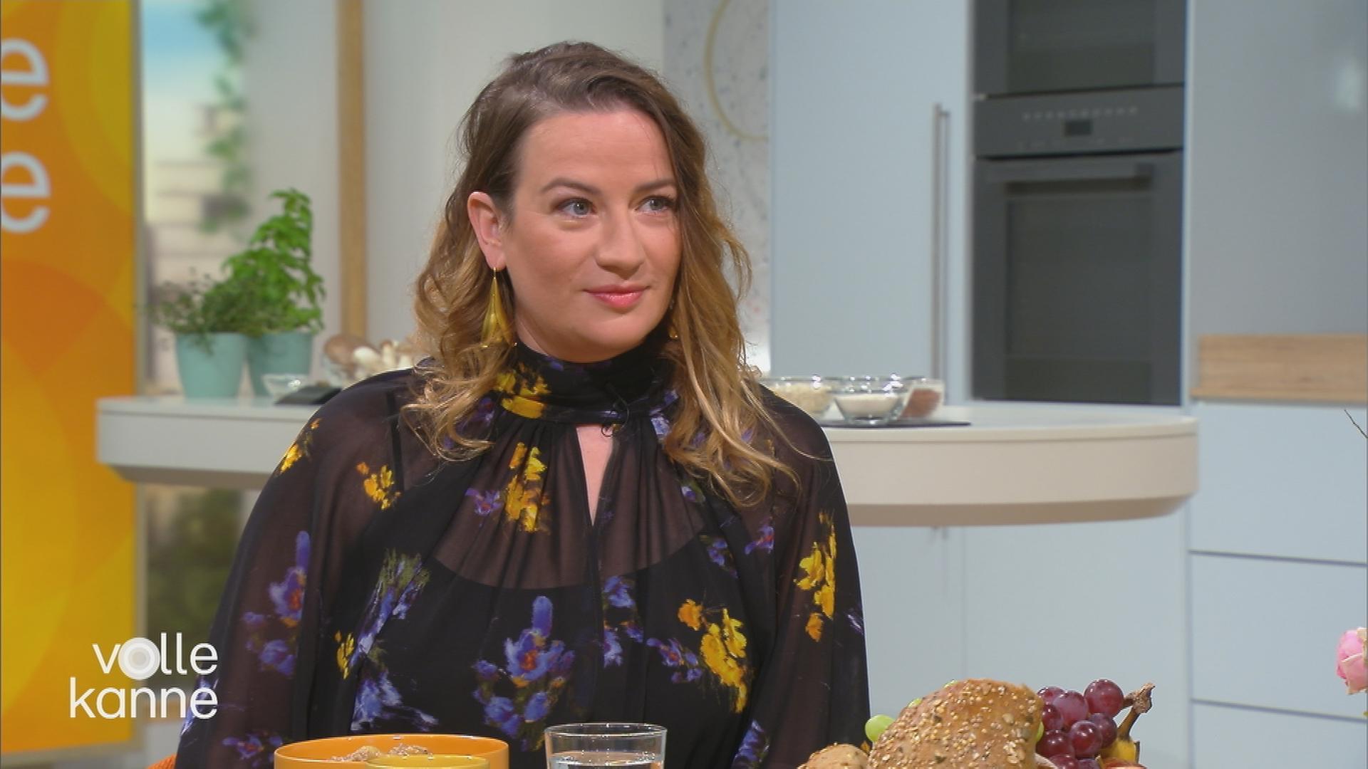 Die Schauspielerin Nina Gummich sitzt mit offenen Haaren am Tisch. 