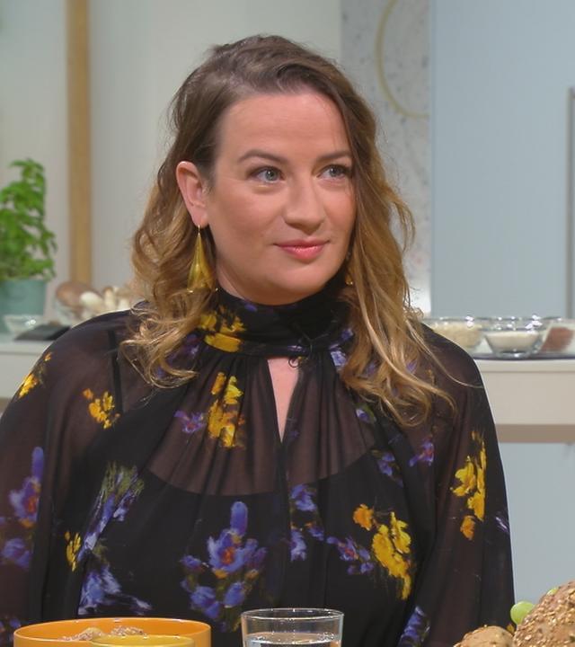 Die Schauspielerin Nina Gummich sitzt mit offenen Haaren am Tisch. 