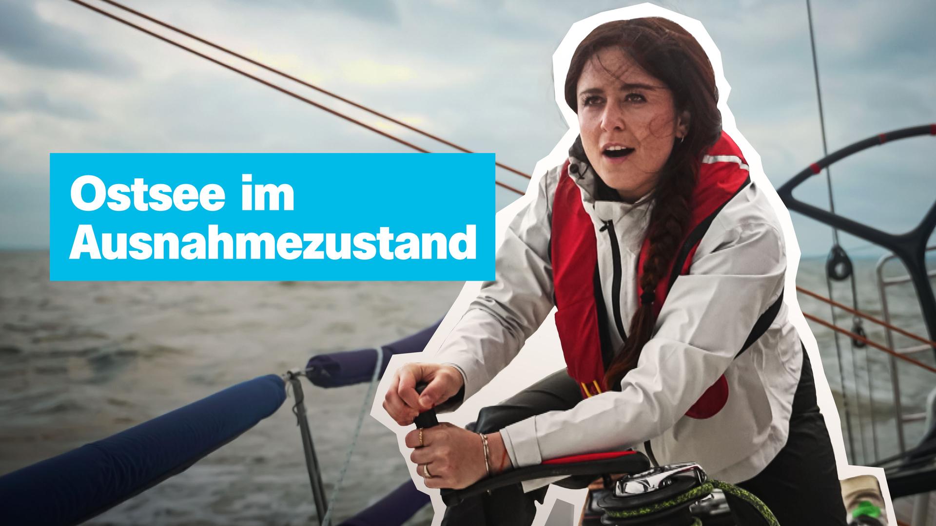 Auf einem Segelboot bei stürmischer See sitzt eine junge Frau in heller Jacke und roter Rettungsweste und kurbelt an einer Kurbel. 