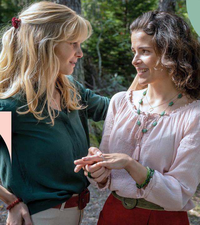 Liv (links) unterhält sich mit ihrer Schwester Smilla (rechts), die nervös mit dem Ring an ihrer Hand spielt. Im Hintergrund ist ein Wald zu sehen.