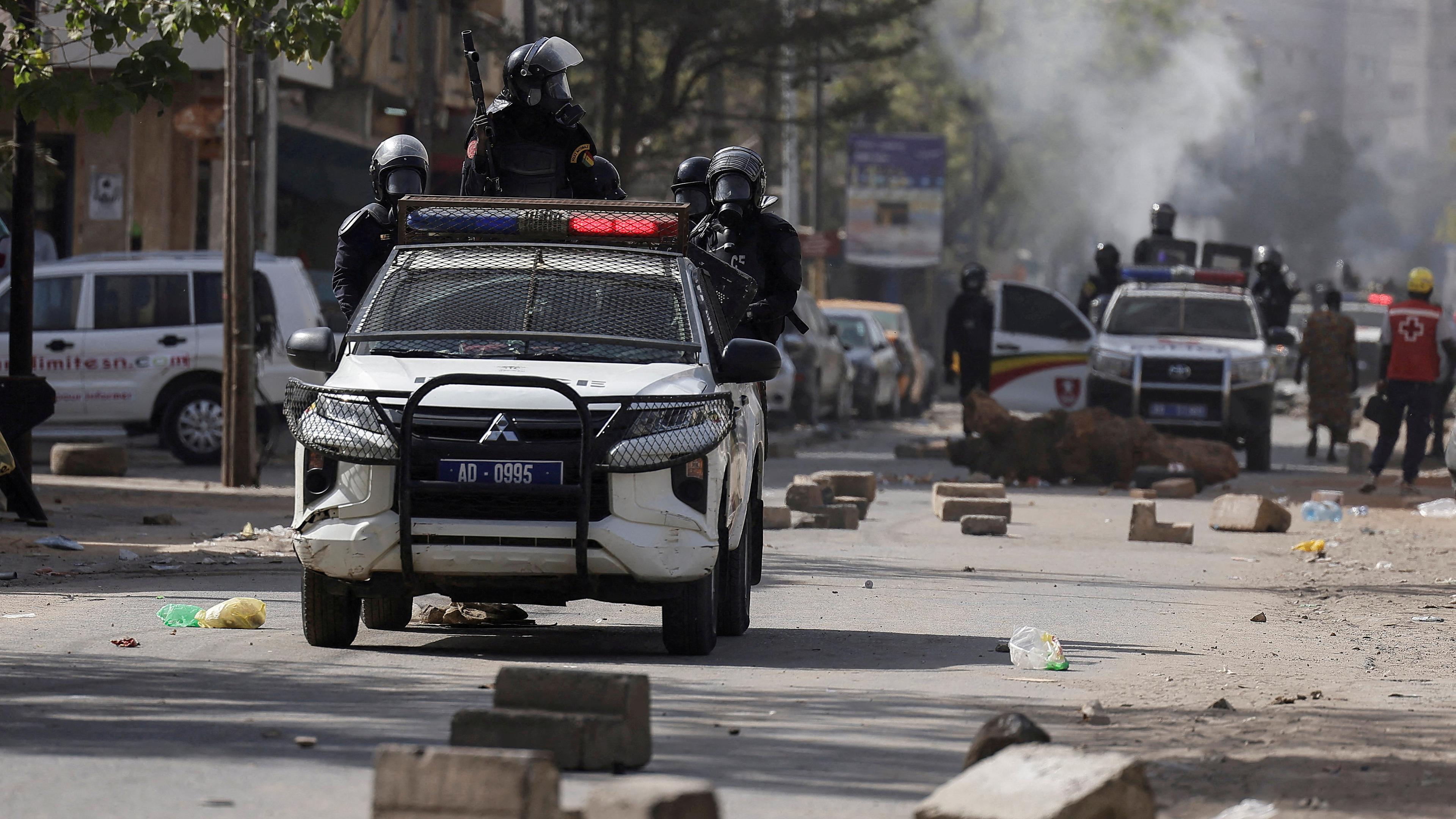 Polizeiautos fahren im senegalesischen Dakar durch eine Straße auf der Steinblöcke liegen. 