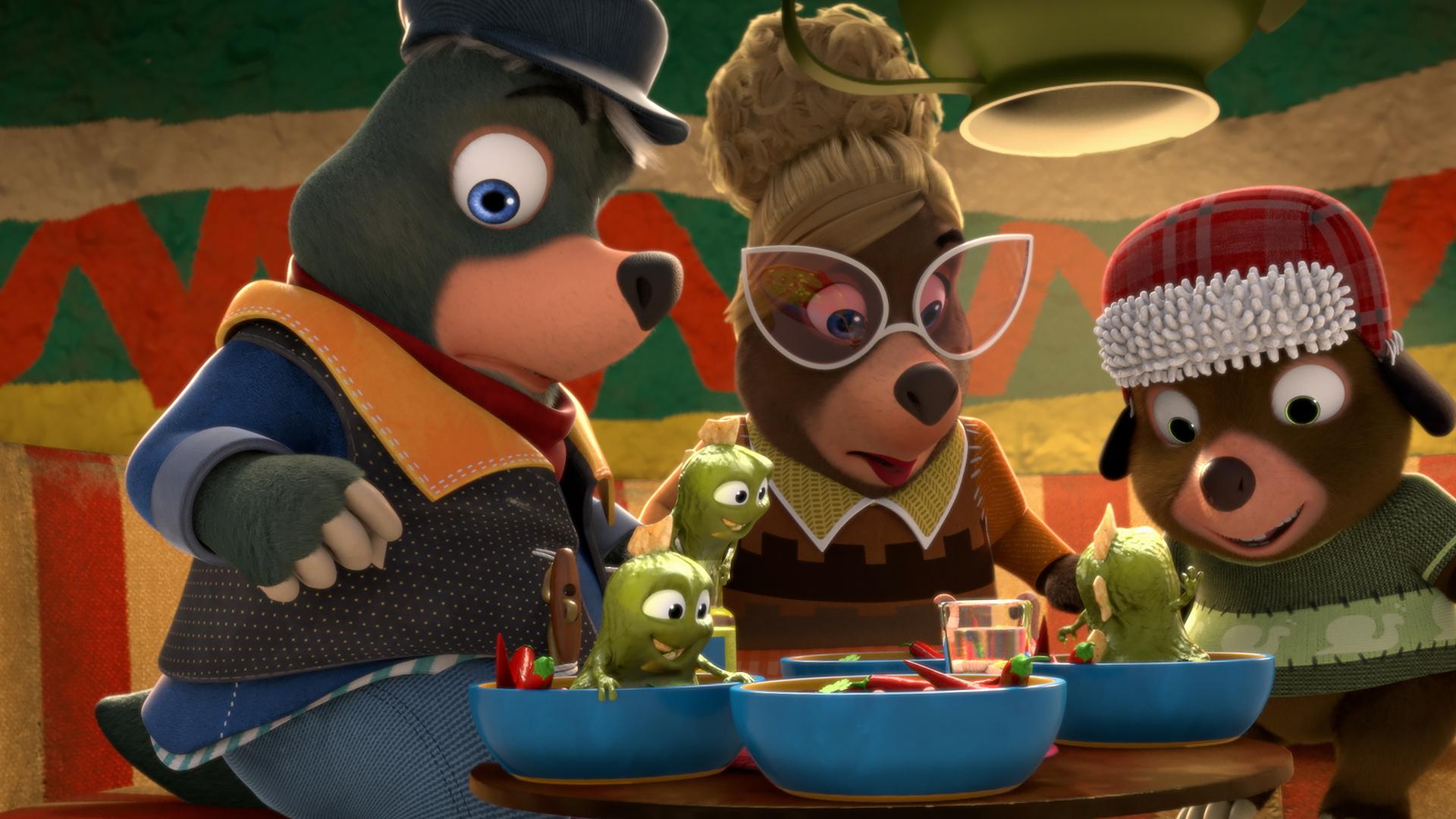 An einem Tisch in Señora Marias Restaurant sitzen drei Gäste und blicken erstaunt auf ihre Teller. Dort tauchen aus der Chilisoße kleine, grüne, schleimige Wesen auf.