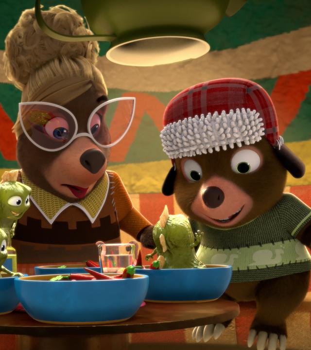 An einem Tisch in Señora Marias Restaurant sitzen drei Gäste und blicken erstaunt auf ihre Teller. Dort tauchen aus der Chilisoße kleine, grüne, schleimige Wesen auf.