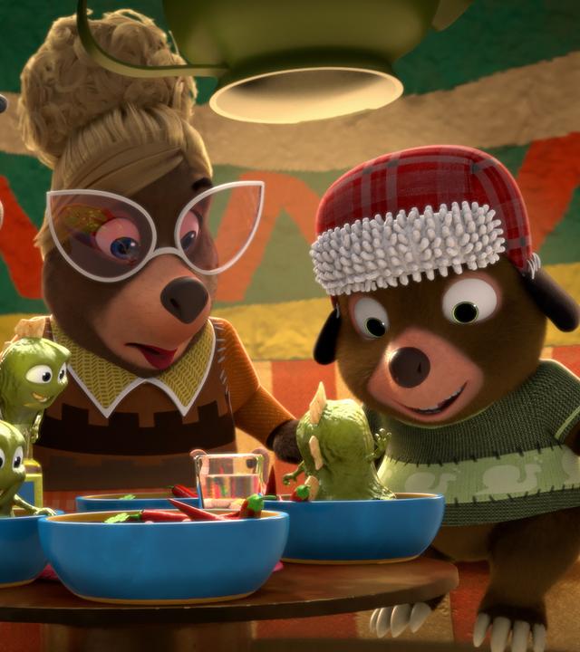 An einem Tisch in Señora Marias Restaurant sitzen drei Gäste und blicken erstaunt auf ihre Teller. Dort tauchen aus der Chilisoße kleine, grüne, schleimige Wesen auf.