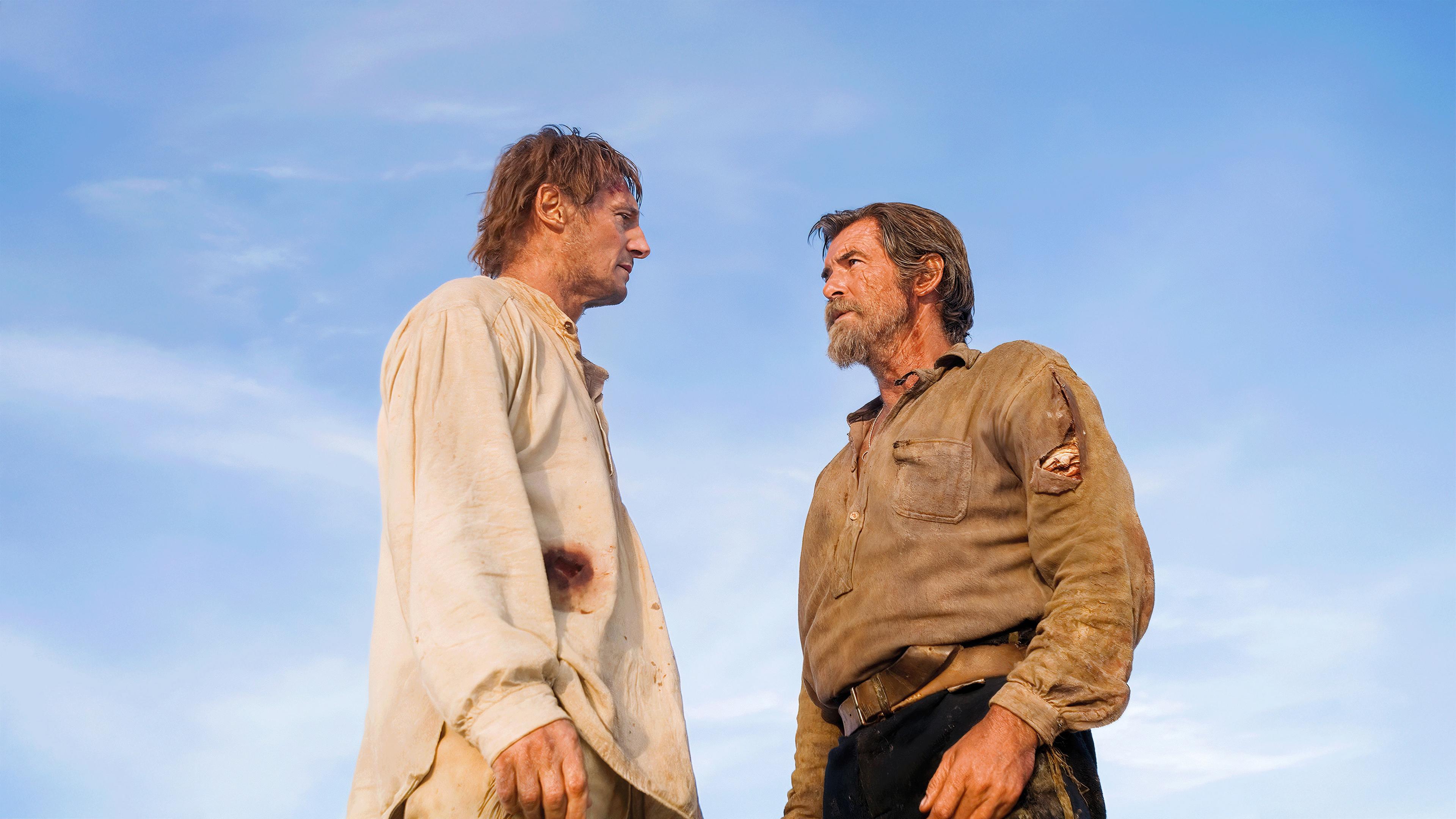 Carver und Gideon stehen sich in zerschlissener Kleidung gegenüber, bereit für eine Konfrontation, mit einem weiten blauen Himmel im Hintergrund.