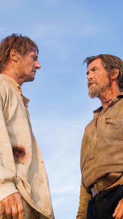 Carver und Gideon stehen sich in zerschlissener Kleidung gegenüber, bereit für eine Konfrontation, mit einem weiten blauen Himmel im Hintergrund.