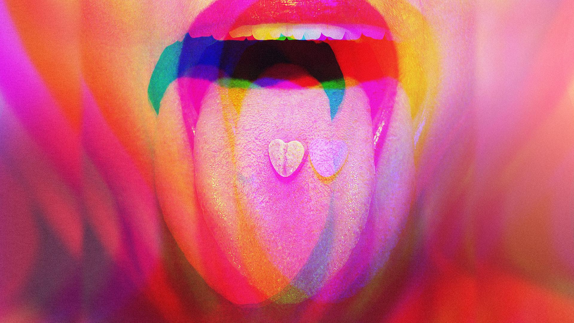 Nahaufnahme eines geöffneten Mundes mit ausgestreckter Zunge; darauf liegt eine kleine herzförmige Pille, überlagert von bunten, verschwommenen Farbeffekten.