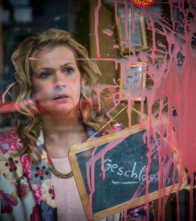 Notruf Hafenkante - Shopping": Nina Hell (Tina Amon Amonsen) steht mit schockiertem Blick hinter einer Fensterscheibe, auf der ein großer Klecks rote Farbe klebt.