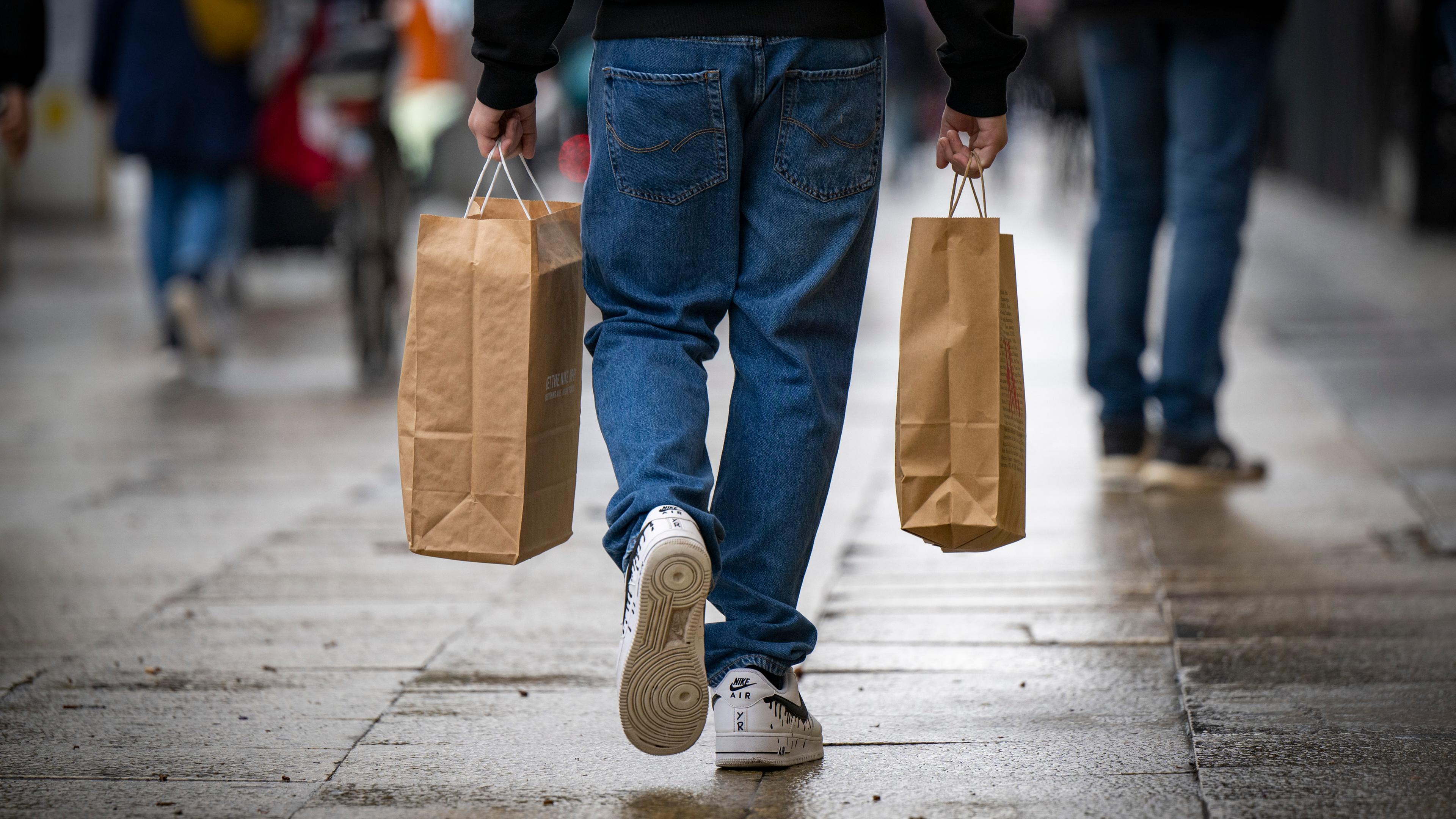 Ein Mann geht über eine Straße in Berlin und trägt zwei Einkaufstaschen.