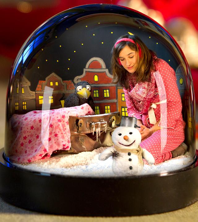 Rudi, Koffer, Schneemann und Frau Siebenstein sitzen in einer Schneekugel