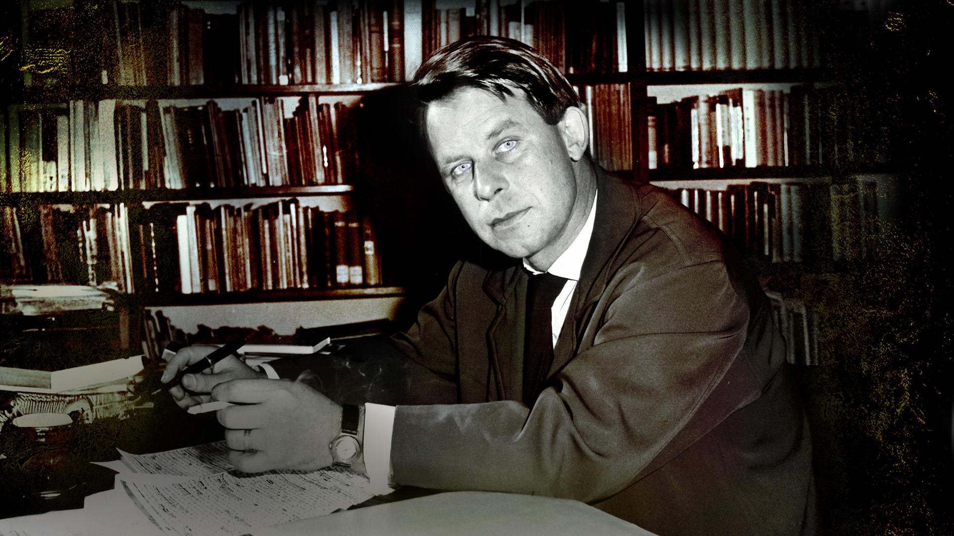  Der junge Siegfried Lenz sitzt vor einer Bücherwand am Schreibtisch (s/w). 